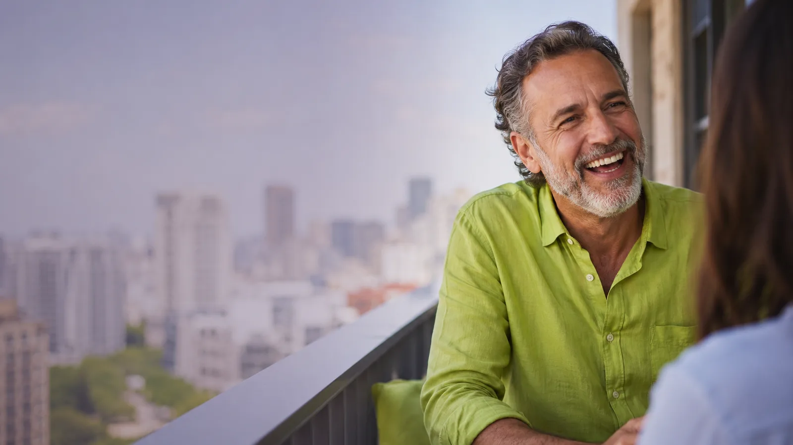 Man in his late fifties laughing on a city balcony