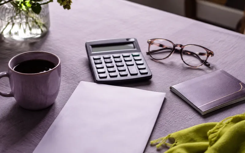 Kitchen table with calculator, reading glasses, coffee and a passport