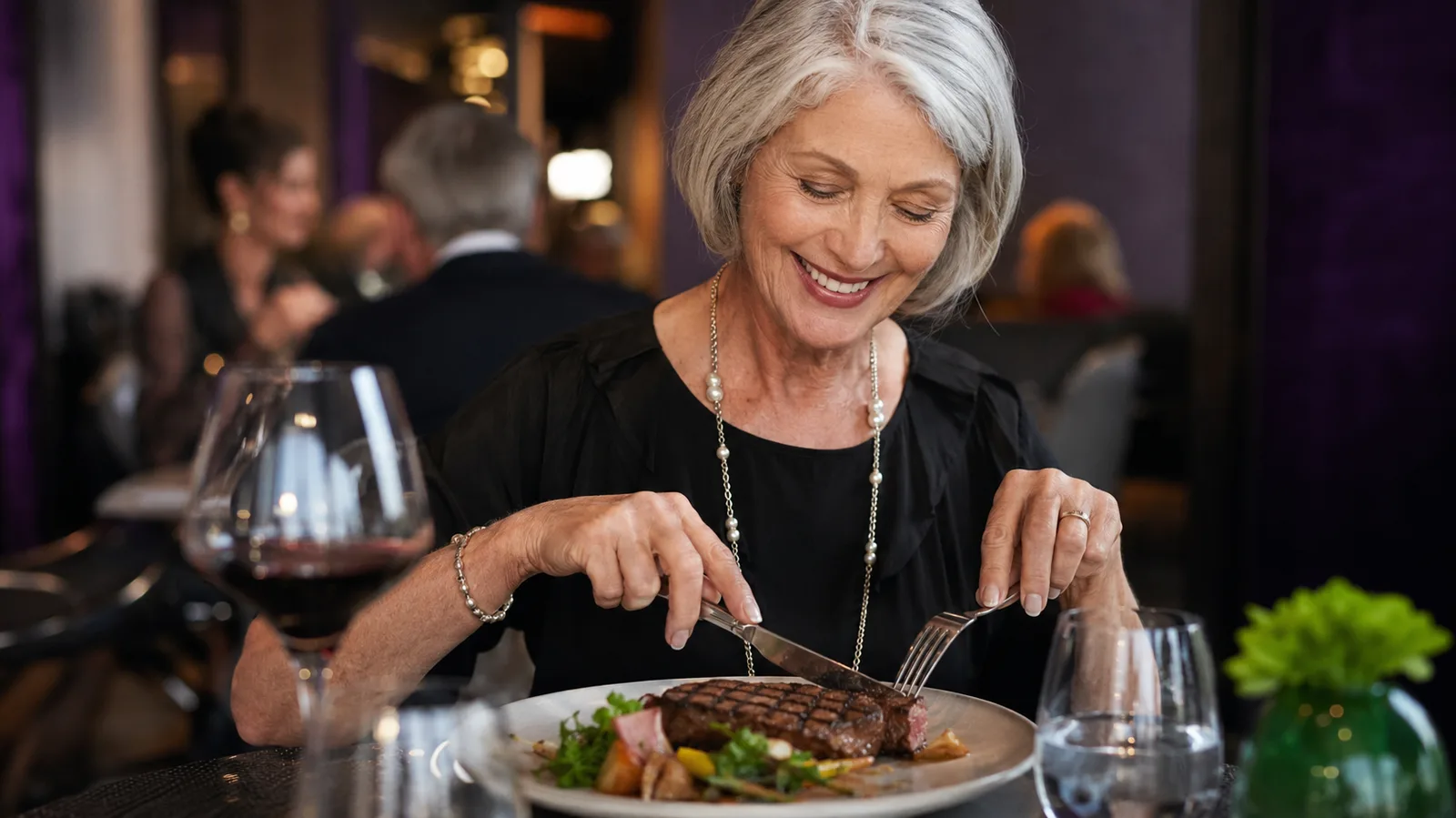 Woman in her sixties smiling while cutting a steak at a restaurant table